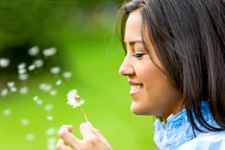 Hermosa mujer soplando una flor y sonriendo